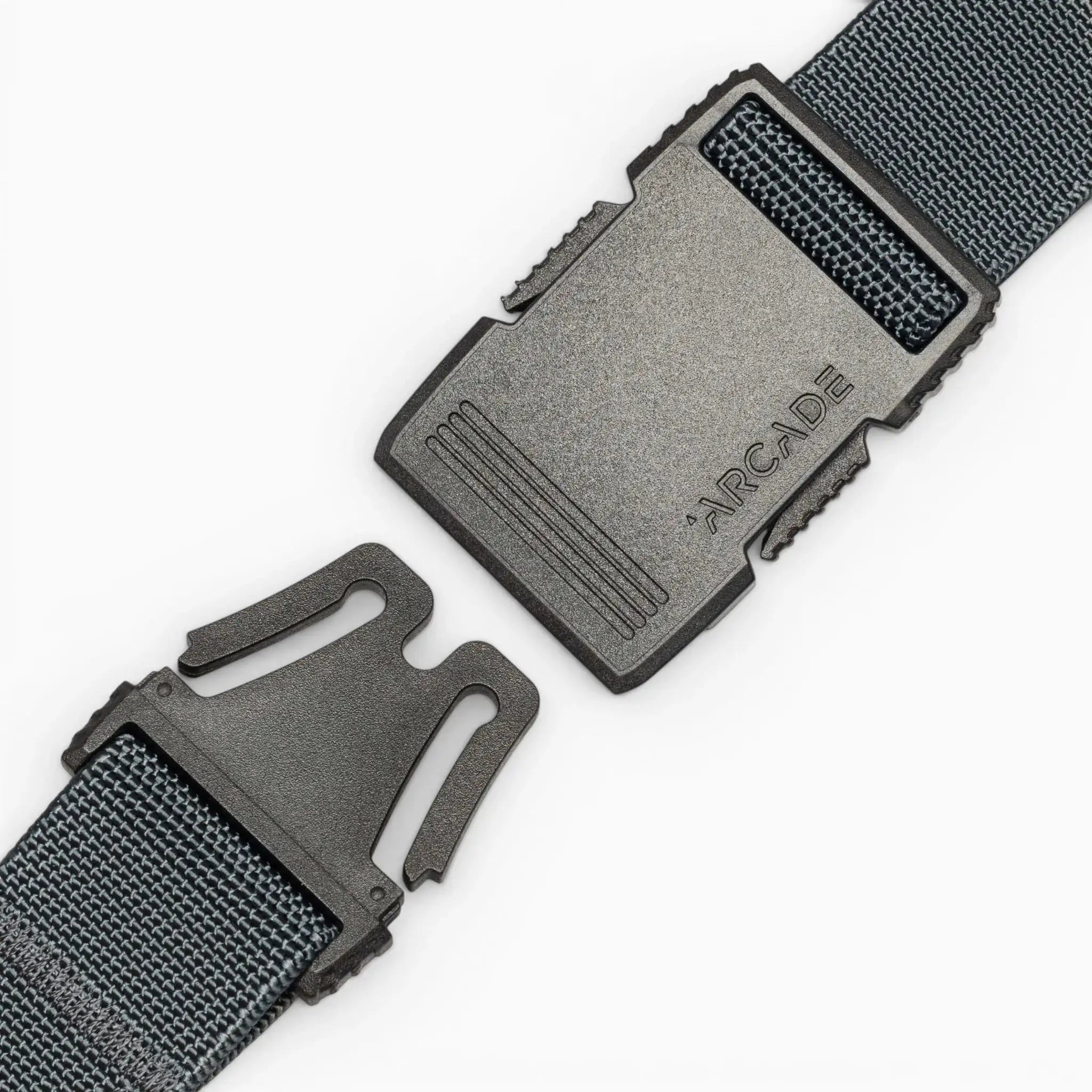 A close-up of a black plastic buckle on a dark woven strap, partially unclipped, with ARCADE engraved. The Arcade Belts Hardware belt stands out for its superior strength against a plain white background.