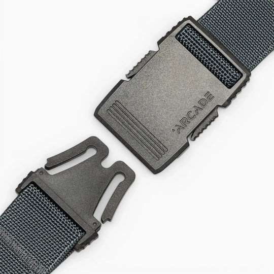 A close-up of a black plastic buckle on a dark woven strap, partially unclipped, with ARCADE engraved. The Arcade Belts Hardware belt stands out for its superior strength against a plain white background.