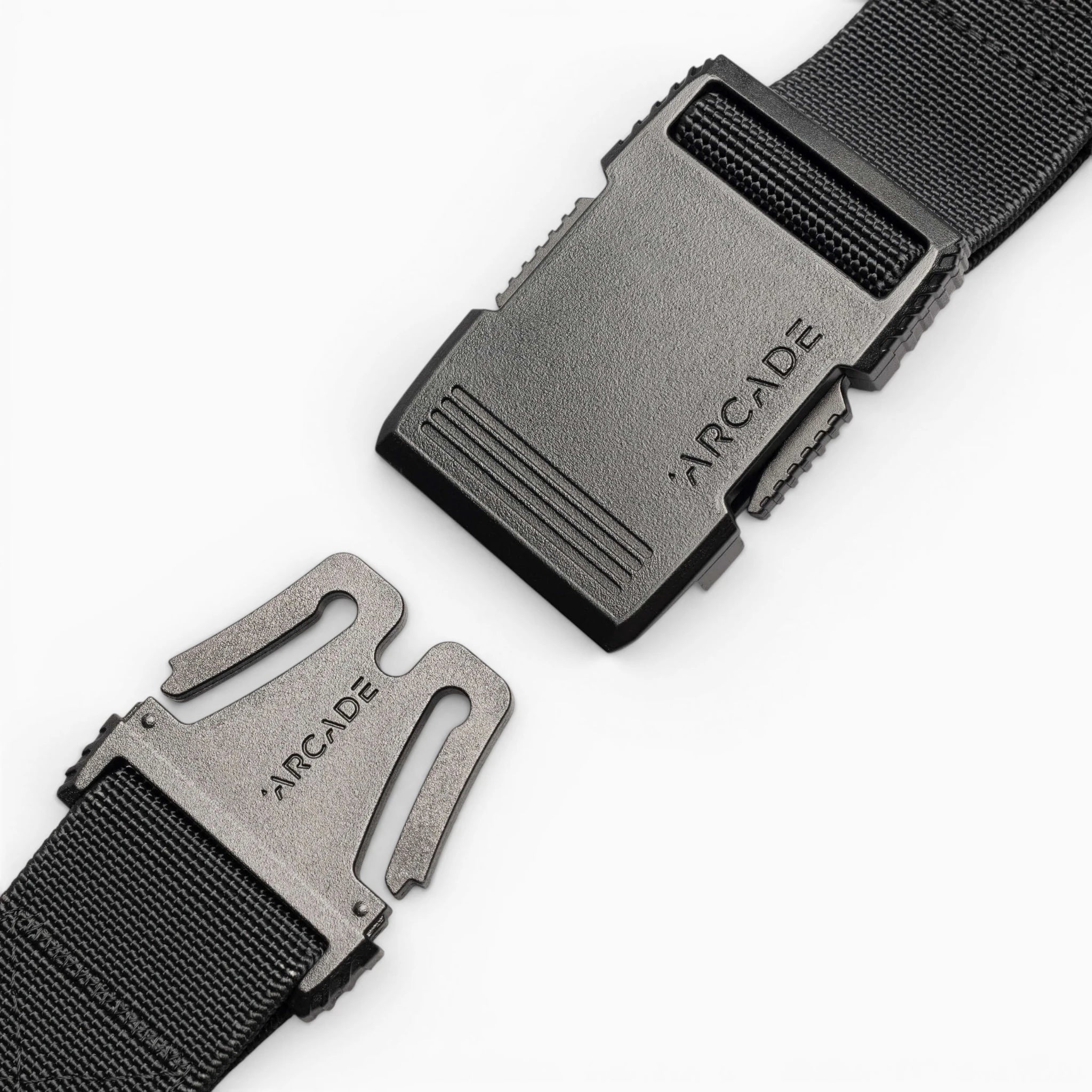 Close-up of the Arcade Belts Hardware black stretch belt with a plastic buckle, partially unclasped. Both buckle pieces are engraved with ARCADE. The sleek, low profile design is highlighted against a plain white background.