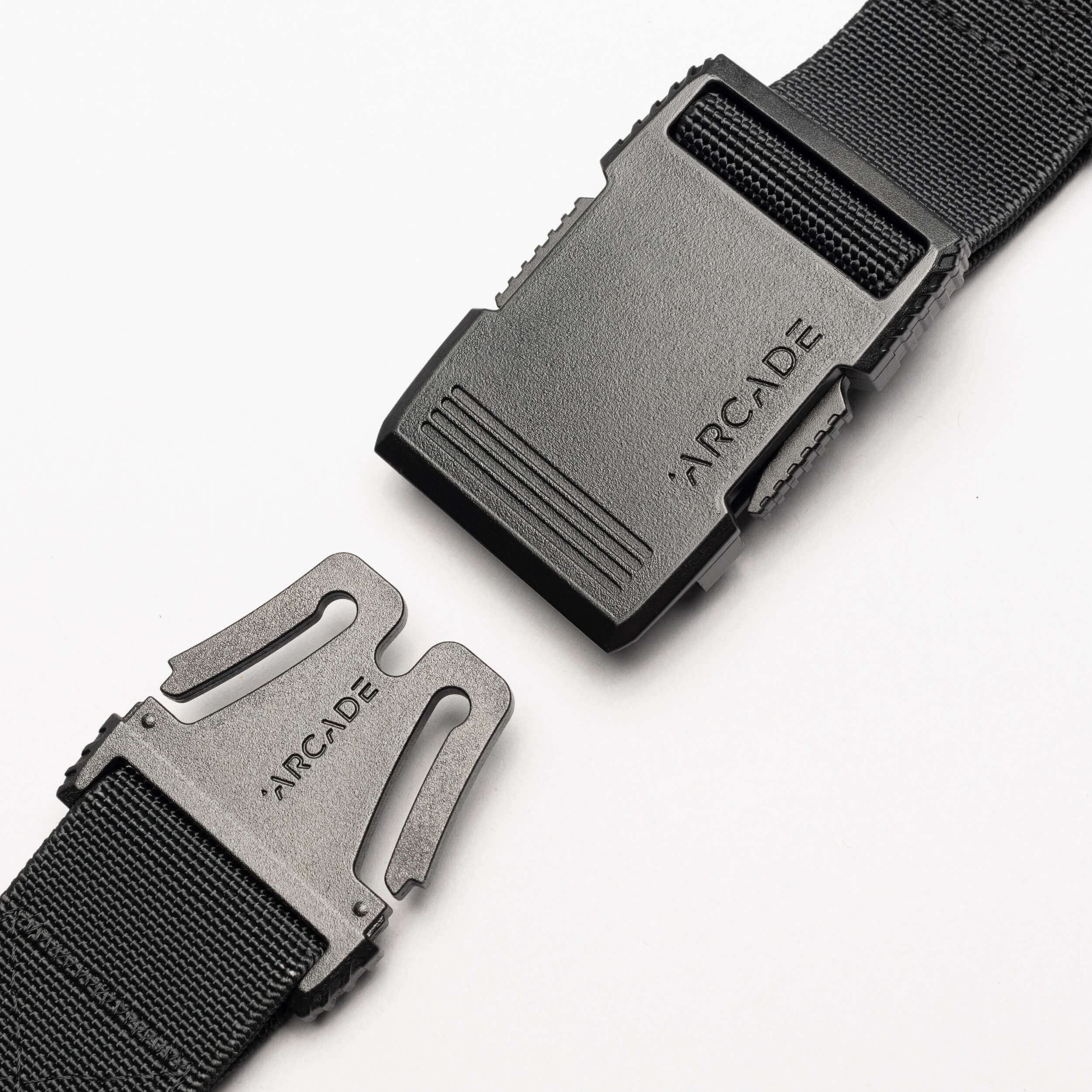A close-up of the Arcade Belts Utility Long Kit, a black elastic stretch belt with a plastic buckle showing the brand name engraved on both clasp and buckle, displayed against a white background.