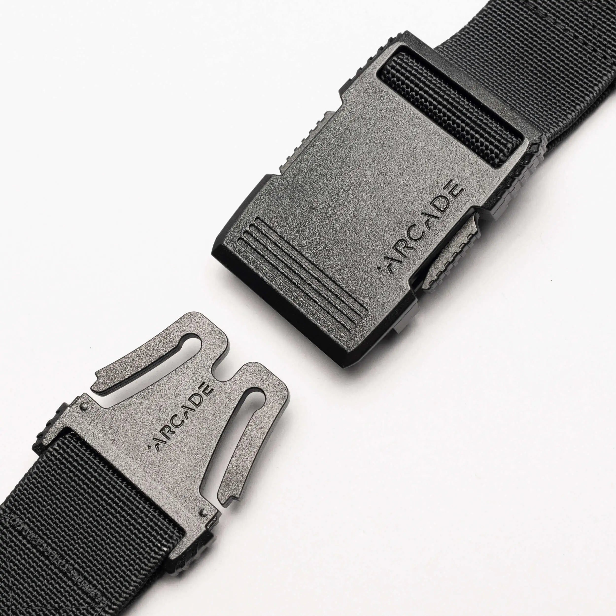 A close-up of the Arcade Belts Utility Long Kit, a black elastic stretch belt with a plastic buckle showing the brand name engraved on both clasp and buckle, displayed against a white background.