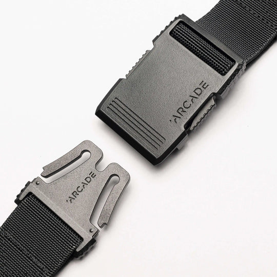 A close-up of the Arcade Belts Utility Long Kit, a black elastic stretch belt with a plastic buckle showing the brand name engraved on both clasp and buckle, displayed against a white background.