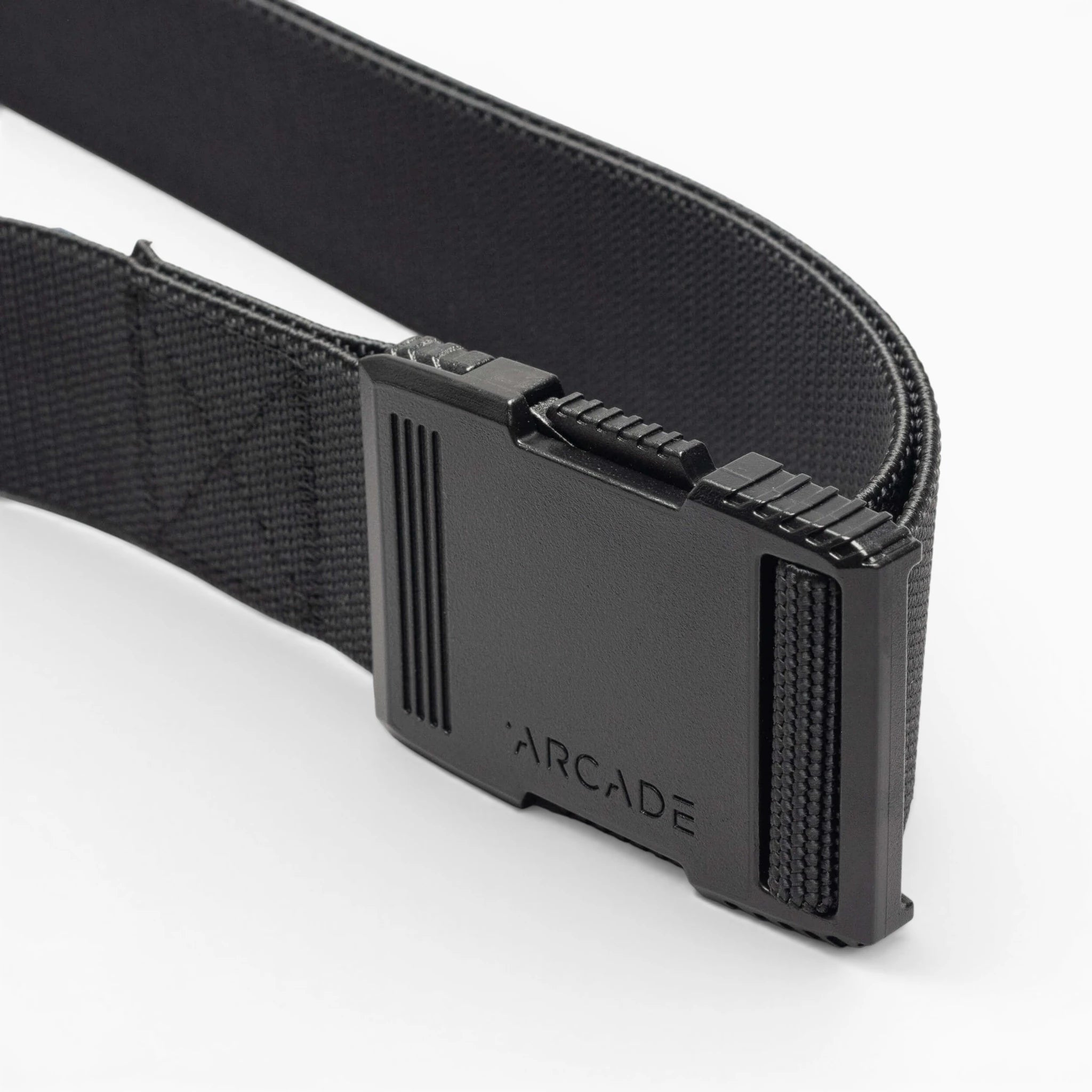 A close-up of the Arcade Belts Hardware: a black elastic stretch belt with a rectangular black plastic buckle engraved with “ARCADE,” shown against a white background.