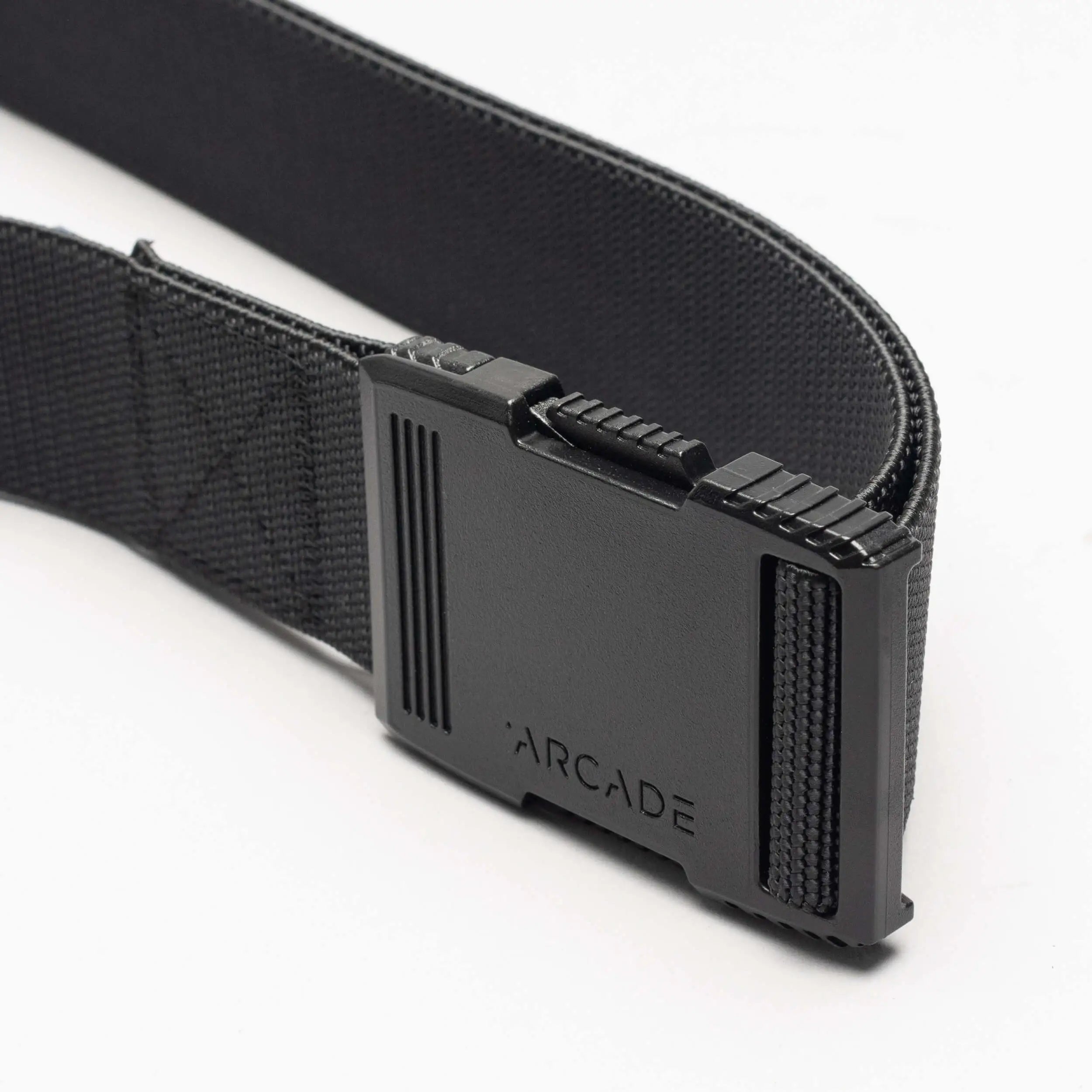 A close-up of the Arcade Belts Hardware: a black elastic stretch belt with a rectangular black plastic buckle engraved with “ARCADE,” shown against a white background.