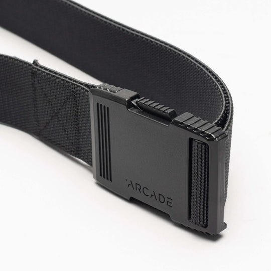 A close-up of the Arcade Belts Hardware: a black elastic stretch belt with a rectangular black plastic buckle engraved with “ARCADE,” shown against a white background.