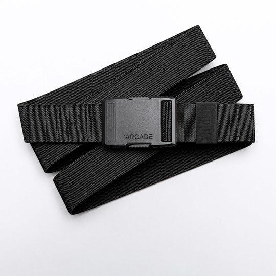 The Arcade Belts Hardware is a black elastic stretch belt with a low profile buckle engraved with ARCADE, neatly coiled on a white background.