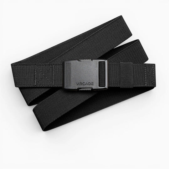 The Arcade Belts Hardware is a black elastic stretch belt with a low profile buckle engraved with ARCADE, neatly coiled on a white background.