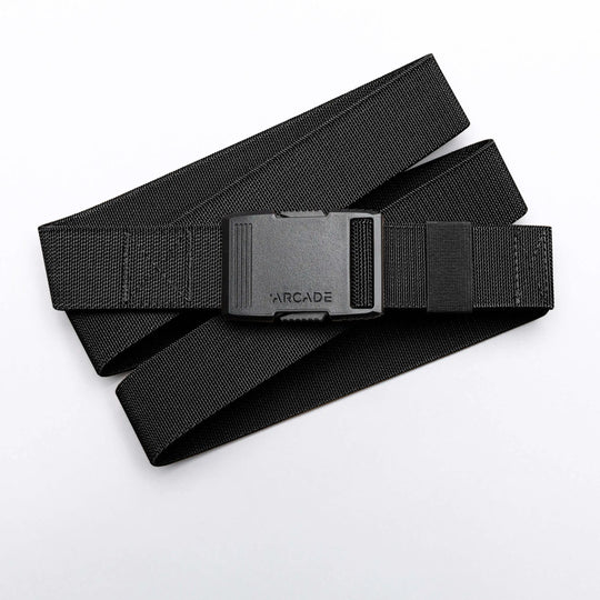 The Arcade Belts Hardware is a black elastic stretch belt with a low profile buckle engraved with ARCADE, neatly coiled on a white background.