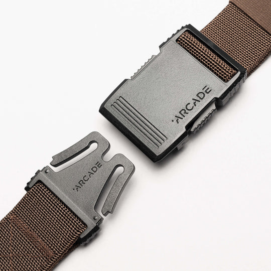 A close-up of the brown Arcade Belts Hardware belt with a black plastic buckle, both pieces engraved with ARCADE, displayed against a white background.