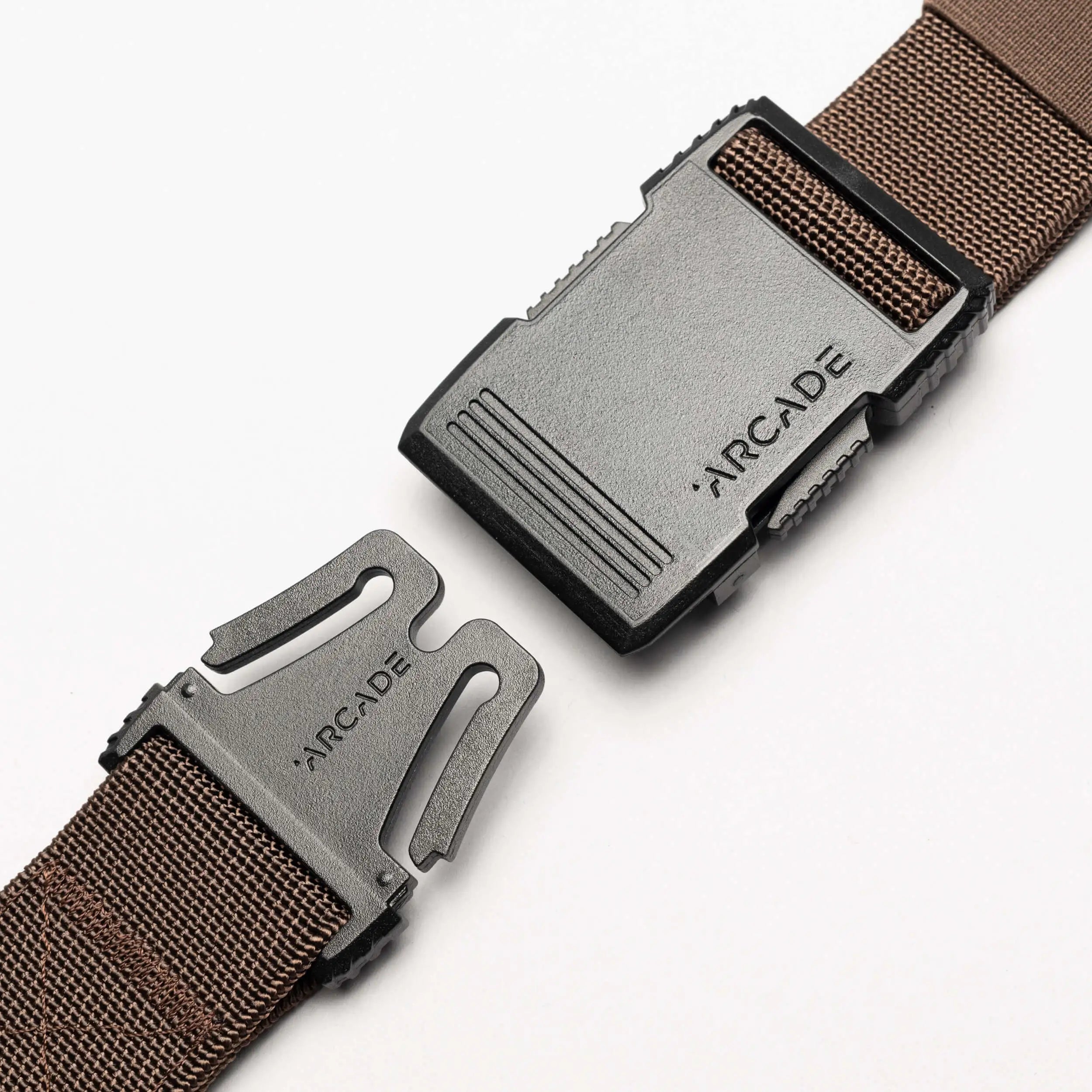 A close-up of the brown Arcade Belts Hardware belt with a black plastic buckle, both pieces engraved with ARCADE, displayed against a white background.