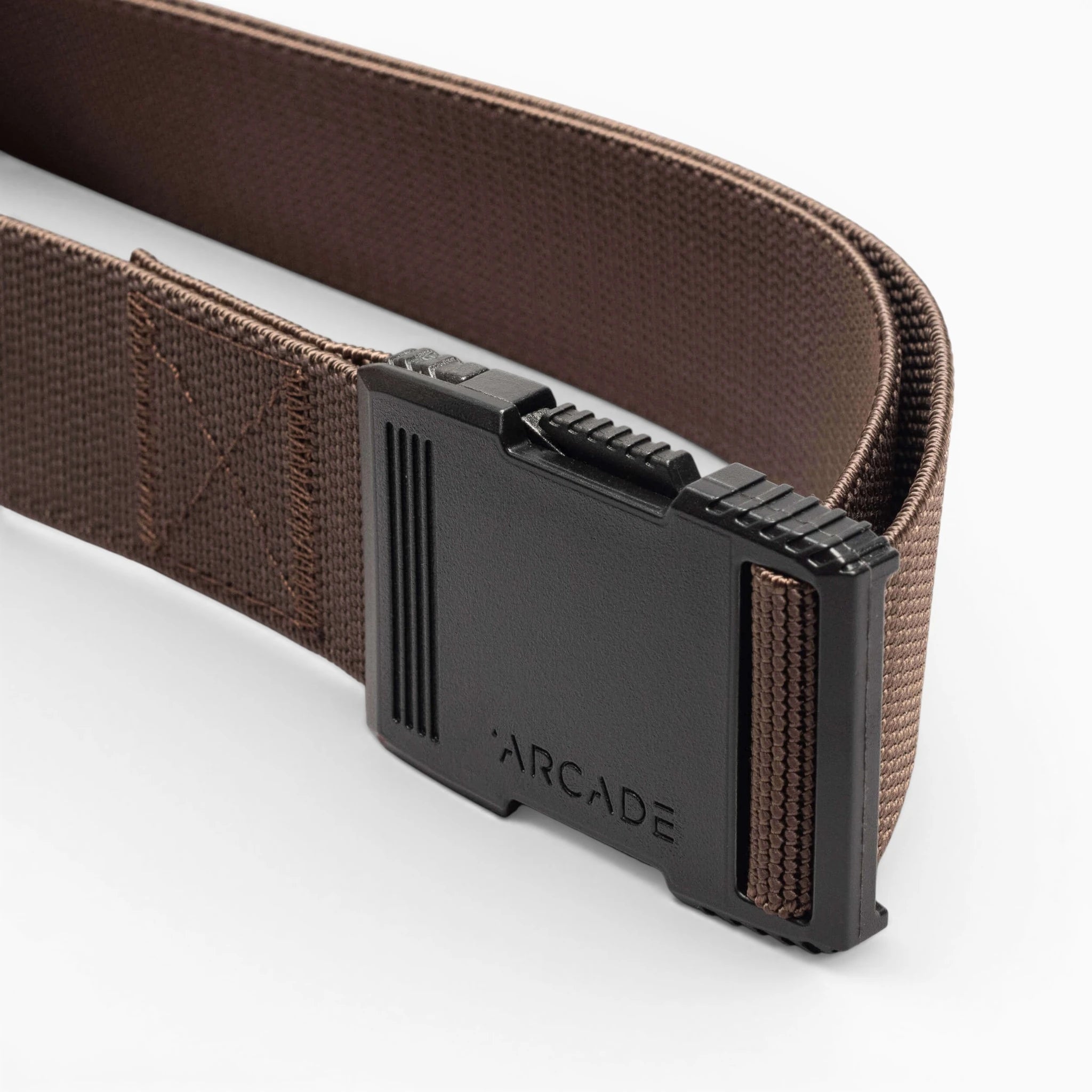 A close-up of the Arcade Belts Hardware belt in brown, showing its black plastic buckle with ridged edges and an embossed ARCADE logo. The elastic stretch belt is displayed on a white background.
