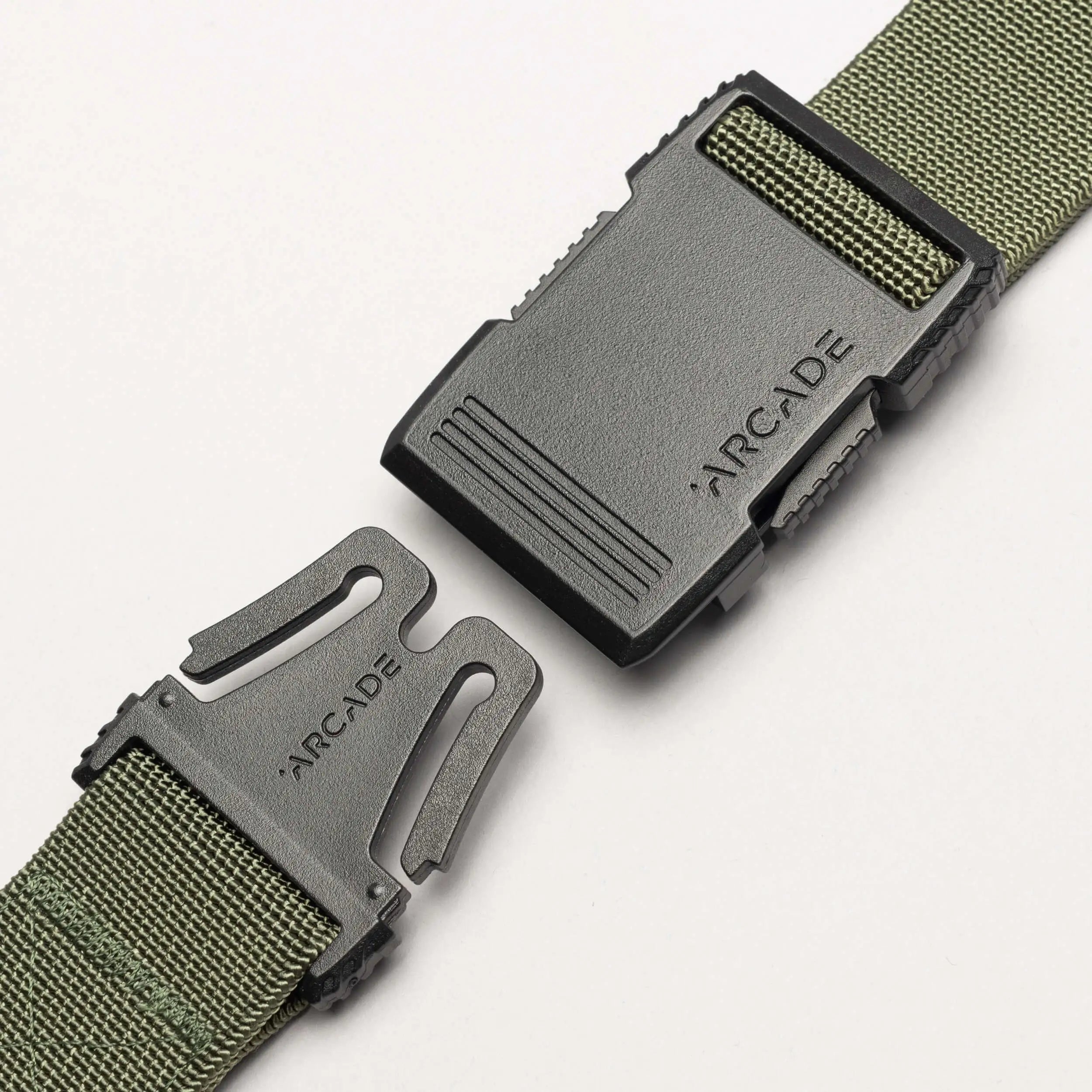 A close-up of the Arcade Belts Hardware, a green woven travel belt with stretch webbing and a black plastic buckle branded ARCADE on both halves, partially unfastened on a white background.