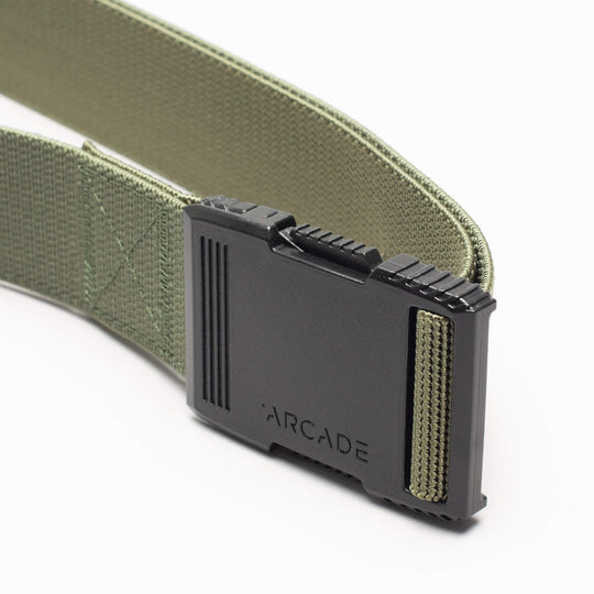 A close-up of the olive green Arcade Belts Hardware with a low-profile, black plastic buckle featuring ridged edges and ARCADE engraved on it, set against a plain white background.