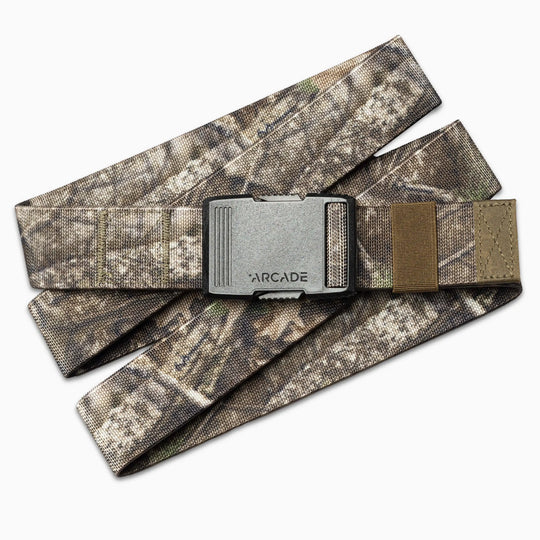 The Arcade Belts Hardware is a camouflage-patterned stretch belt with a rectangular gray metal buckle engraved with ARCADE. The elastic webbing belt is shown in overlapping layers.