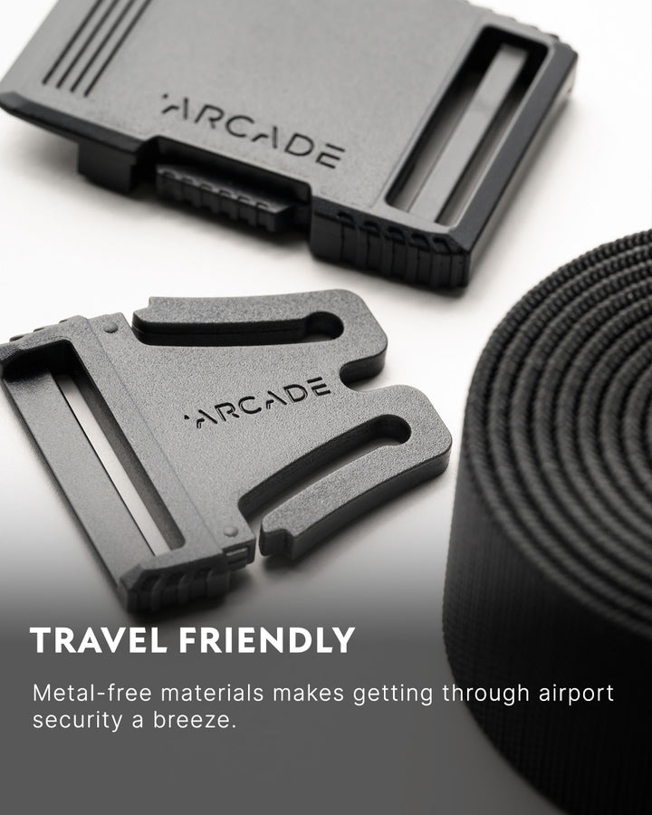 Close-up of a black Elastic Stretch Belt with a metal-free plastic buckle labeled ARCADE. Text reads: Travel Friendly. Metal-free materials and stretch webbing make this travel belt perfect for breezing through airport security.