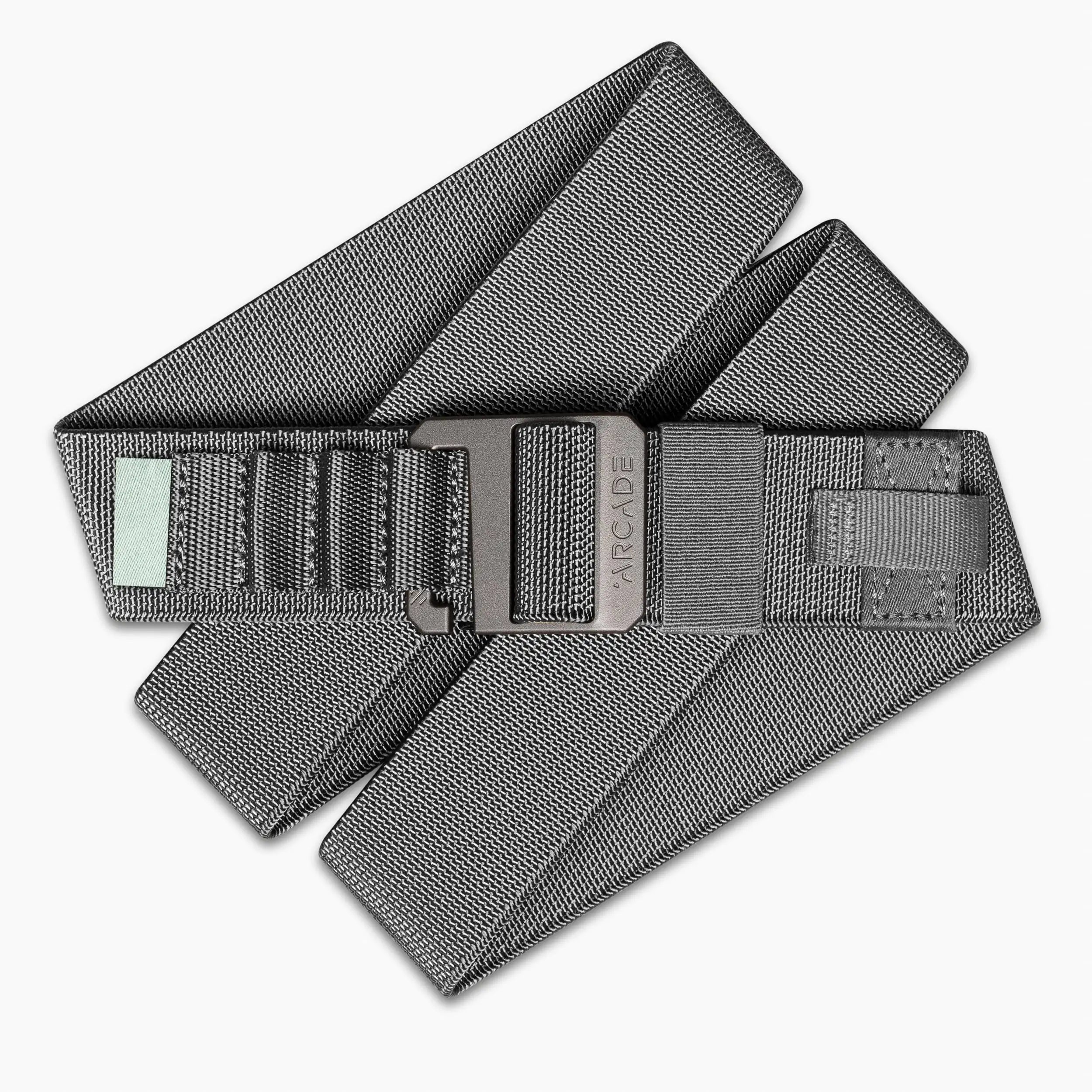 The Arcade Belts Hardware Alu is a gray fabric belt with stretch webbing, a black buckle engraved with Arcade, reinforced stitching, and a small rectangular patch near the buckle. Its neatly coiled and partially folded.