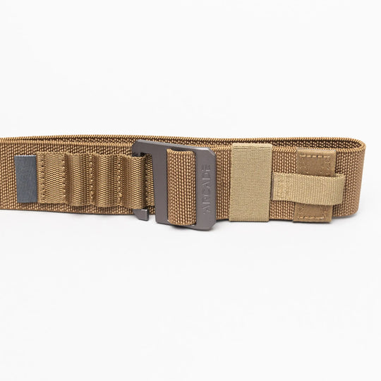 The Arcade Belts Hardware Alu is a tan tactical nylon belt with stretch webbing, reinforced stitching, multiple loops, a Velcro strap, and a sturdy metal buckle, shown laid flat on a white background.