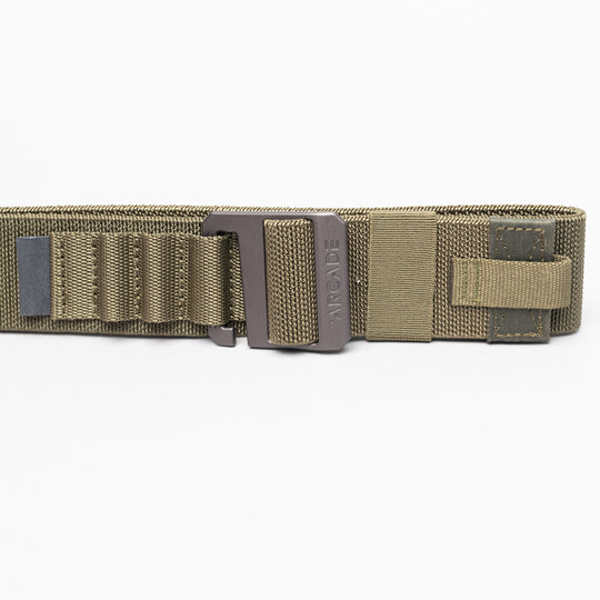 A close-up of the olive green Arcade Belts Hardware Alu tactical belt with a metal buckle, reinforced stitching, webbing loops, and Velcro strap. This low-profile belt offers durability and comfort against a white background.