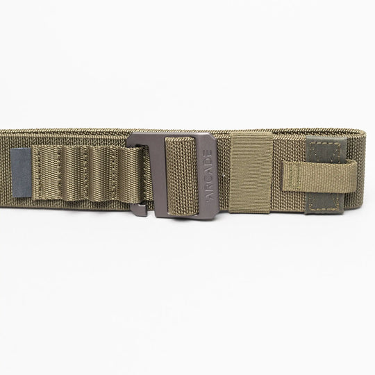 A close-up of the olive green Arcade Belts Hardware Alu tactical belt with a metal buckle, reinforced stitching, webbing loops, and Velcro strap. This low-profile belt offers durability and comfort against a white background.