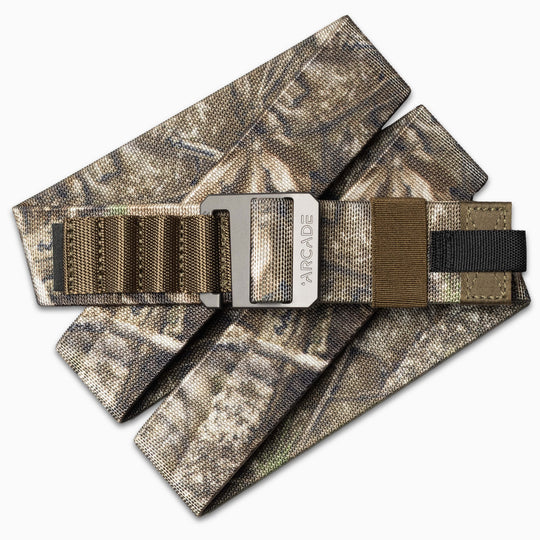 The Arcade Belts Hardware Alu is a camouflage-patterned fabric belt with brown and black webbing, featuring a brushed metal buckle engraved with the brand name for added style.