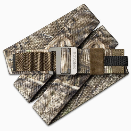 The Arcade Belts Hardware Alu is a camouflage-patterned fabric belt with brown and black webbing, featuring a brushed metal buckle engraved with the brand name for added style.