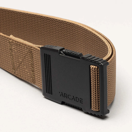 A close-up of the Arcade Belts Hardware: a brown woven belt with a black plastic buckle featuring "ARCADE" engraved on the front, showcasing its superior strength against a plain, light background.