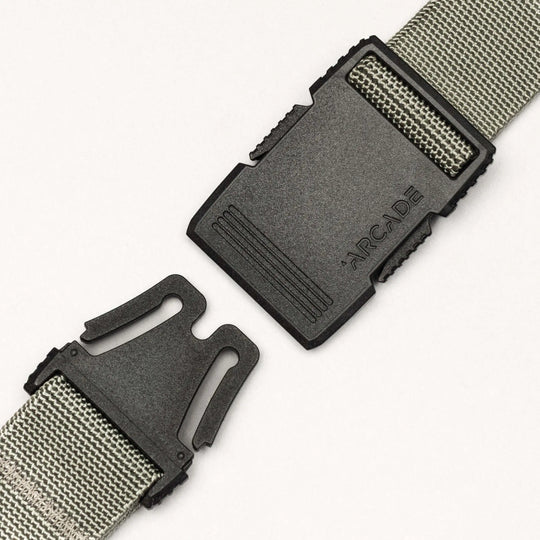 A close-up of the gray Arcade Belts Hardware belt features a black plastic buckle with "ARCADE" embossed, shown partially unclasped against a plain white background.