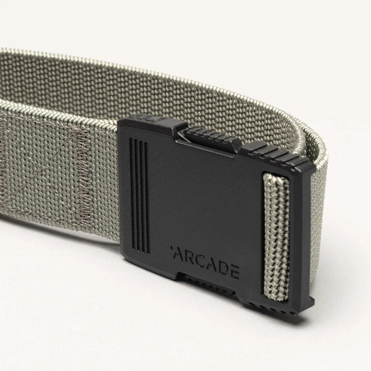 A close-up of the gray Hardware belt by Arcade Belts, featuring superior strength and a black plastic buckle engraved with ARCADE, shown against a light background.