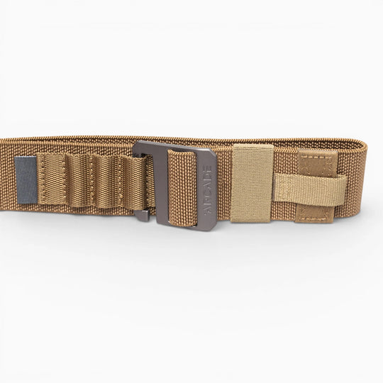 The Arcade Belts Hardware Alu is a tan tactical nylon belt with stretch webbing, reinforced stitching, multiple loops, a Velcro strap, and a sturdy metal buckle, shown laid flat on a white background.