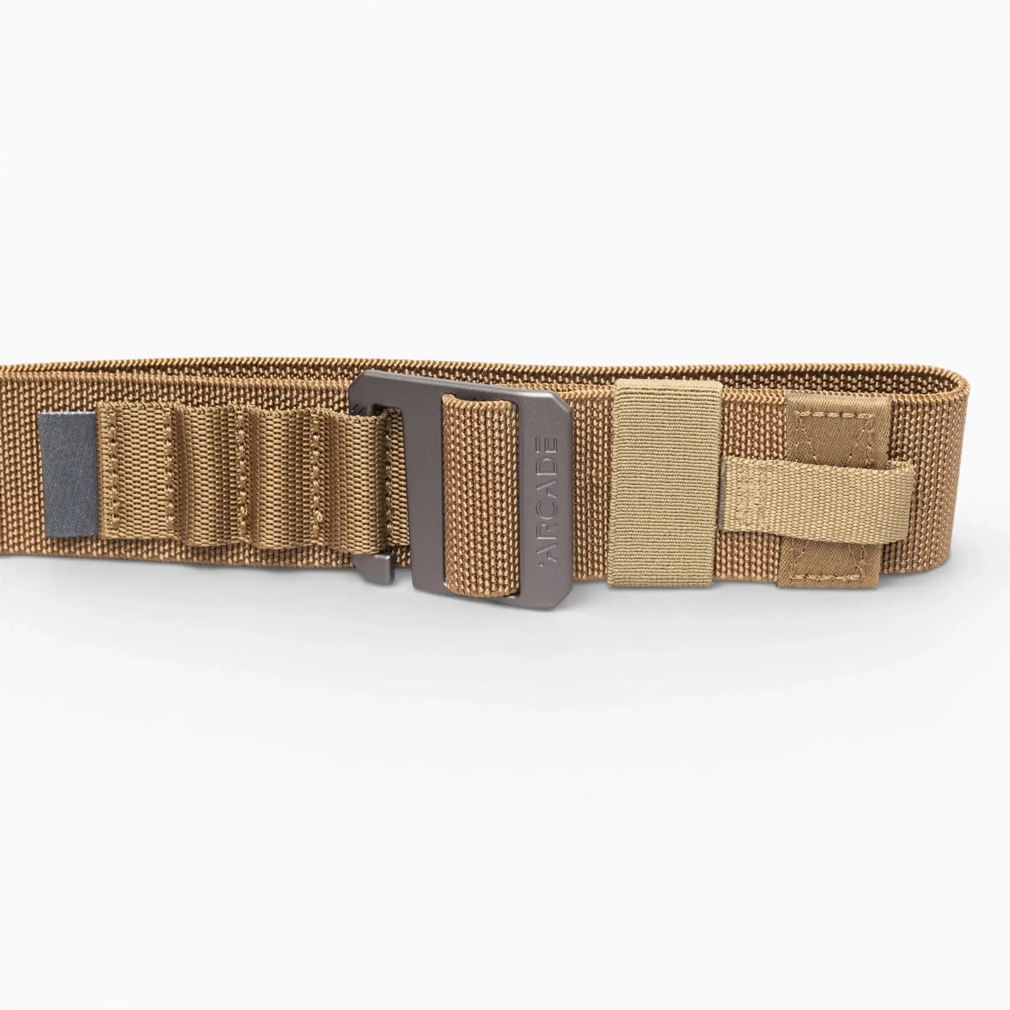 The Arcade Belts Hardware Alu is a tan tactical nylon belt with stretch webbing, reinforced stitching, multiple loops, a Velcro strap, and a sturdy metal buckle, shown laid flat on a white background.