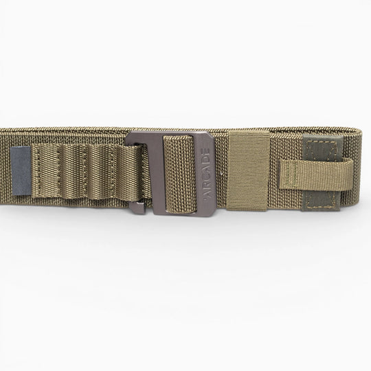 A close-up of the olive green Arcade Belts Hardware Alu tactical belt with a metal buckle, reinforced stitching, webbing loops, and Velcro strap. This low-profile belt offers durability and comfort against a white background.
