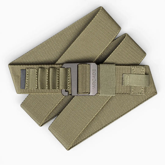 The Hardware Alu by Arcade Belts is an olive green stretch webbing belt with a black metal buckle, ARCADE branding, and reinforced stitching. Its low-profile, layered design makes it perfect for travel and daily use.