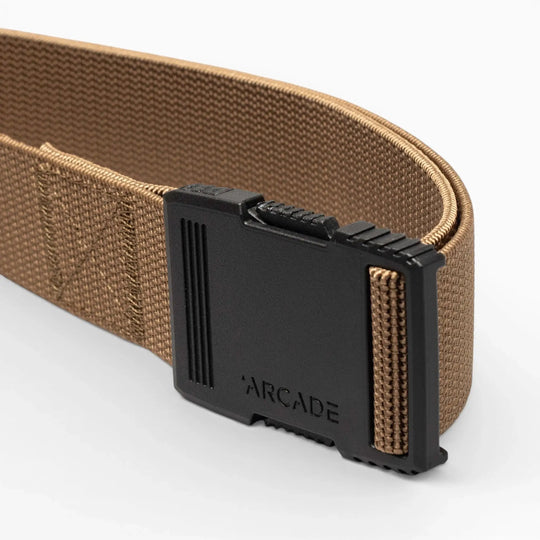 A close-up of the Arcade Belts Hardware: a brown woven belt with a black plastic buckle featuring "ARCADE" engraved on the front, showcasing its superior strength against a plain, light background.