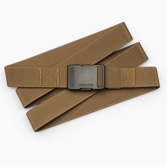 The Arcade Belts Hardware, a tan nylon belt with a black plastic buckle, is displayed in a zigzag pattern on a white background, highlighting its superior strength.