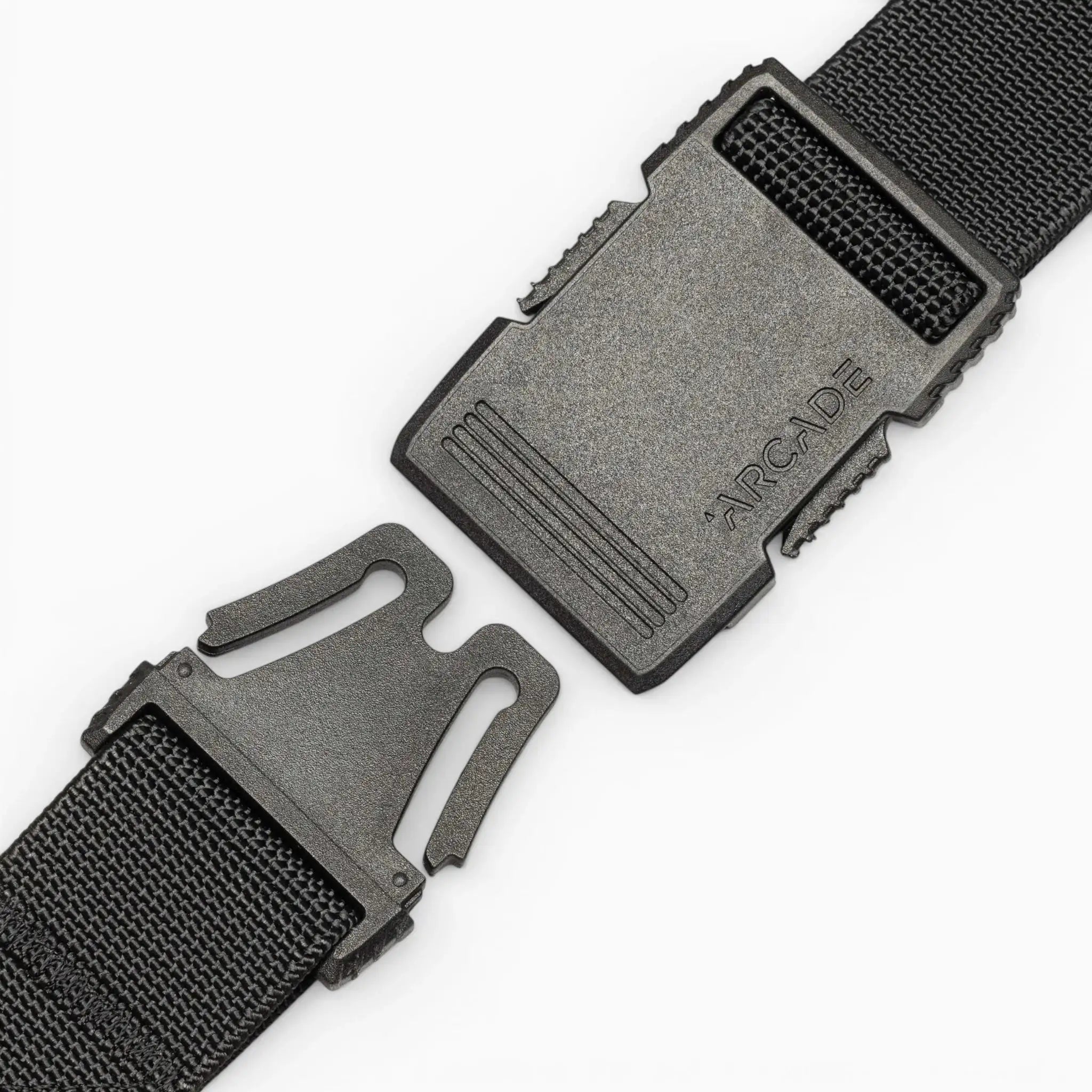 A close-up of a black plastic buckle on the Arcade Belts Hardware strap shows its two ends separated, with "ARCADE" embossed on the top piece. This belt offers superior strength against a clean white background.