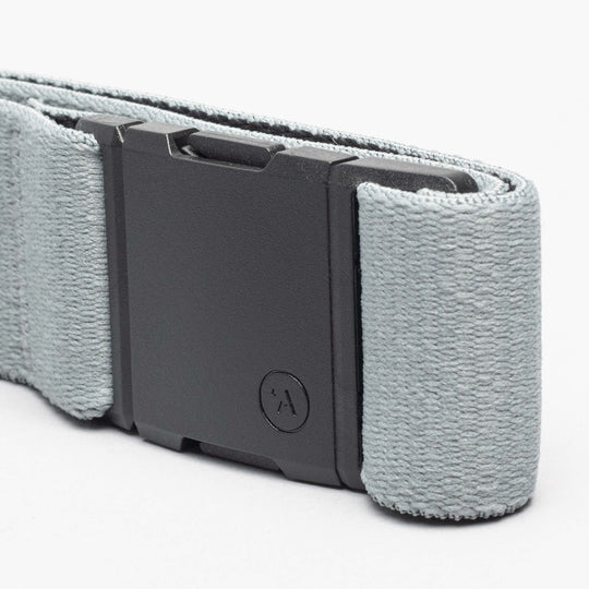 A close-up of an Arcade Belts Island Collection belt in light gray, featuring a low-profile matte black rectangular buckle with a small circular logo and textured stretch webbing fabric.
