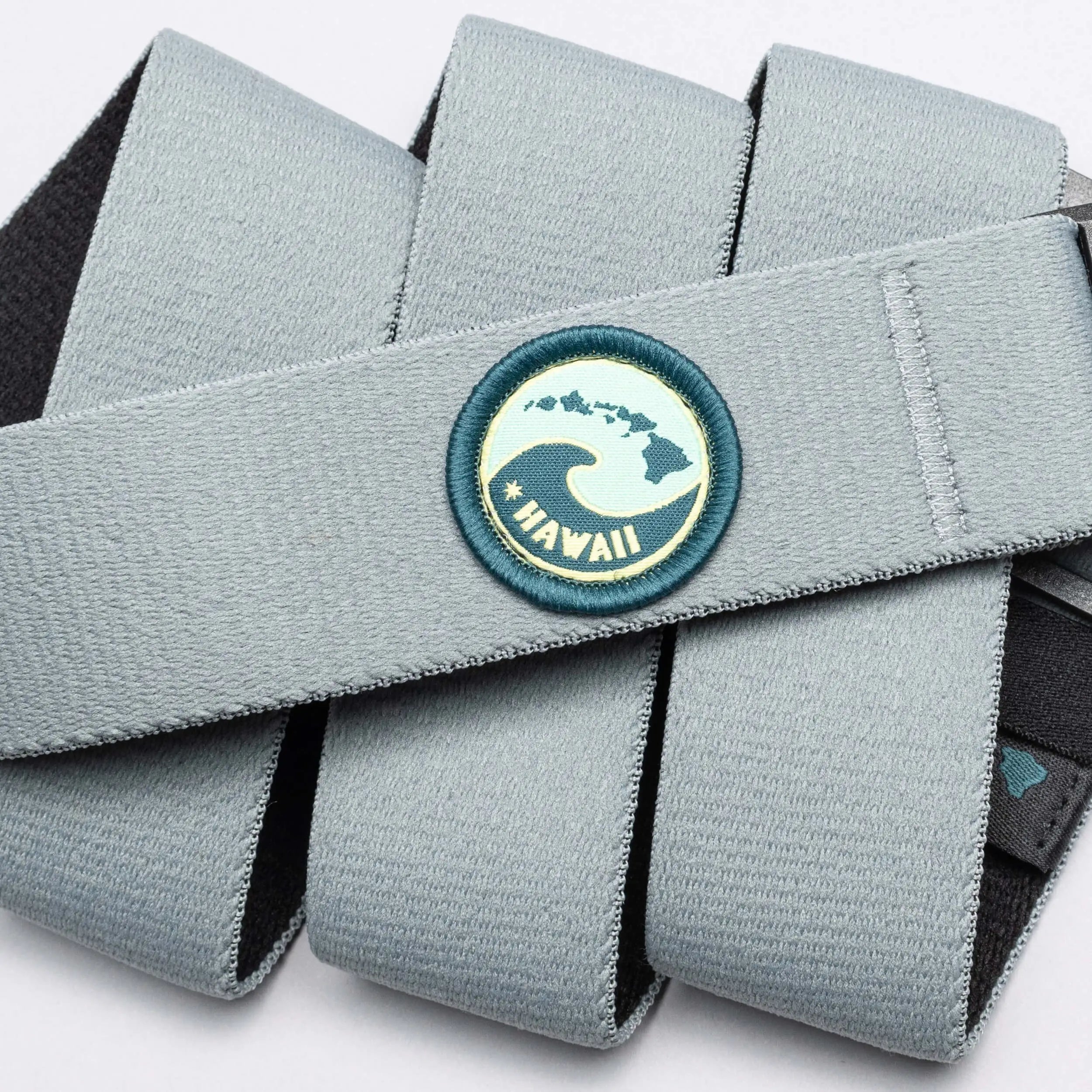 A light gray Arcade Belts Island Collection belt with elastic webbing features a round patch showing a wave, Hawaiian Islands, and 