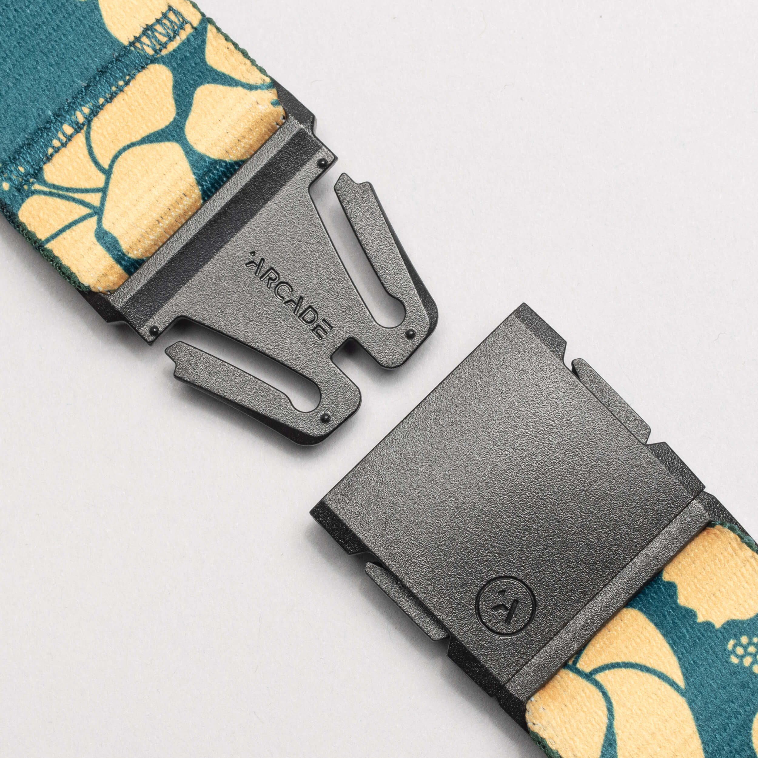 Close-up of a black buckle featuring the Arcade Belts brand, from the Island Collection, with a teal and yellow floral pattern inspired by the Aloha spirit and a simple, modern design.
