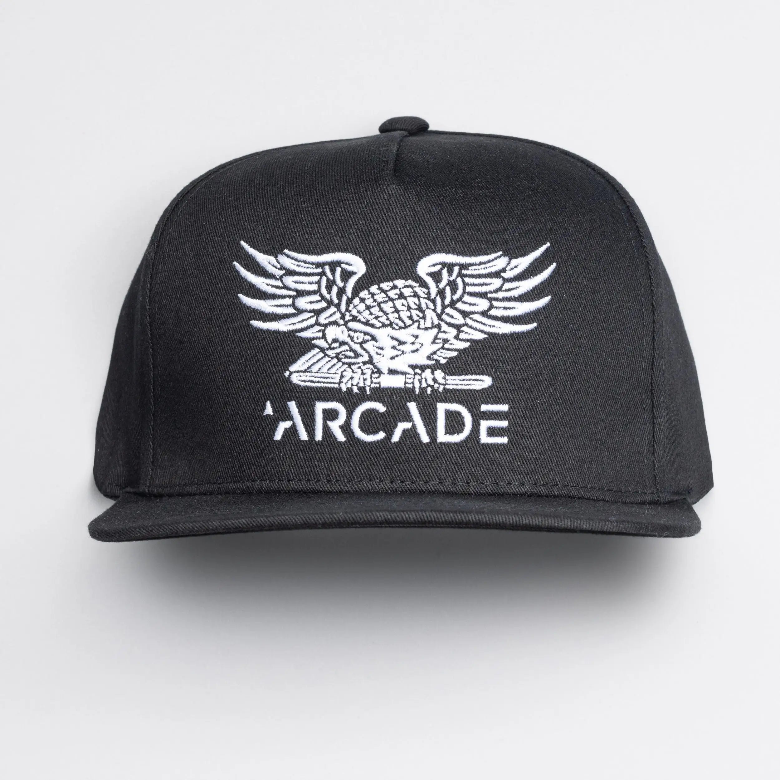 The Arcade High Crown Hat by Arcade Belts is a black snapback featuring a white embroidered eagle above ARCADE on the front, inspired by the brand’s iconic travel belts and stretch webbing. Photographed on a plain white background.