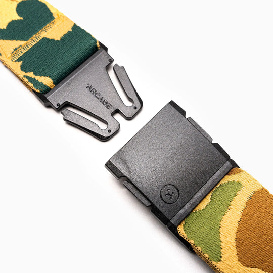 A close-up of the Arcade Belts High Fives Duck Camo, a durable camouflage-patterned belt with a black metal quick-release buckle and ARCADE branding, displayed on a white background—ideal for travel.