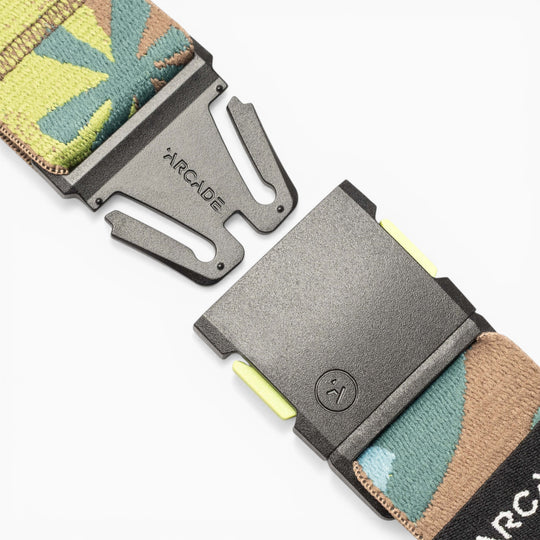 Close-up of the Arcade Belts Inkstorm, a patterned performance stretch webbing belt in green, brown, and tan hues. Partially unclasped, its black plastic A2 buckle displays the ARCADE branding. Designed for flexibility and comfort, this movement-ready belt ensures a perfect fit for any adventure.