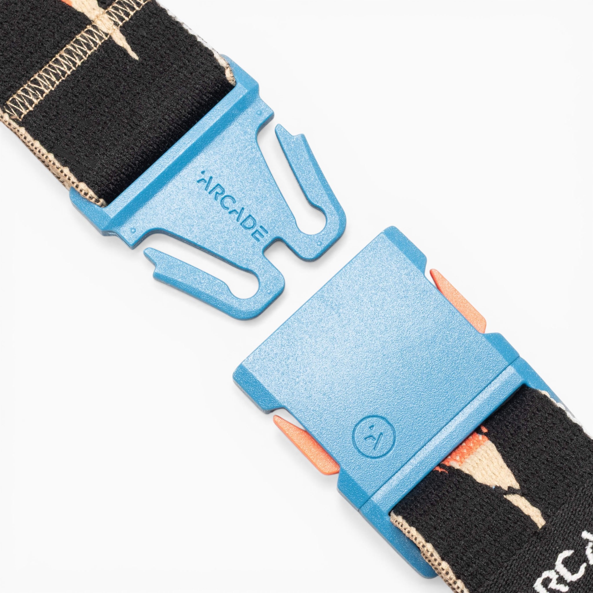 A close-up of the blue plastic A2 buckle, labeled Arcade Belts, attached to the black Inkstorm strap with a tan and orange pattern, highlights the movement-ready design and performance stretch webbing on a white background.