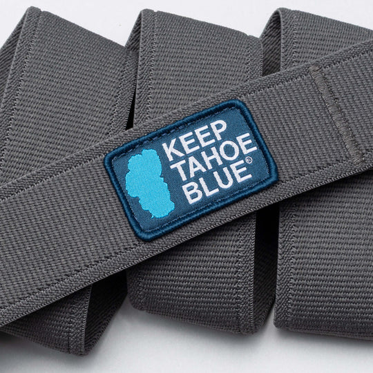 A close-up of the gray fabric Keep Tahoe Blue belt by Arcade Belts, showing a blue patch with KEEP TAHOE BLUE and Lake Tahoe’s silhouette, symbolizing local environmental initiatives.
