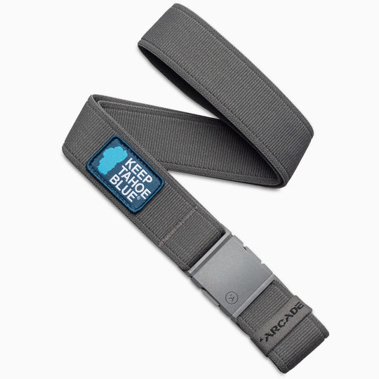 The Arcade Belts Keep Tahoe Blue belt, featuring a patch supporting Lake Tahoe’s environment and a silver buckle, is displayed in a loose loop to promote efforts protecting this iconic destination.