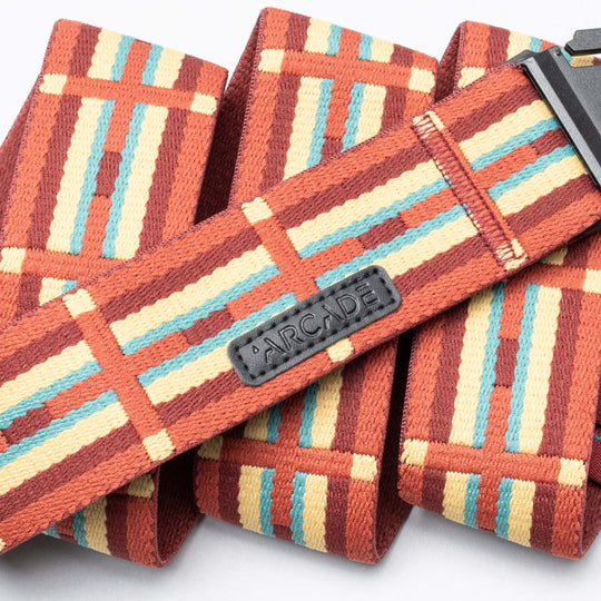 A close-up of the Vernan Kee belt by Arcade Belts, featuring geometric shapes inspired by Navajo rugs in red, yellow, and light blue, with a black Arcade label and black plastic buckle.