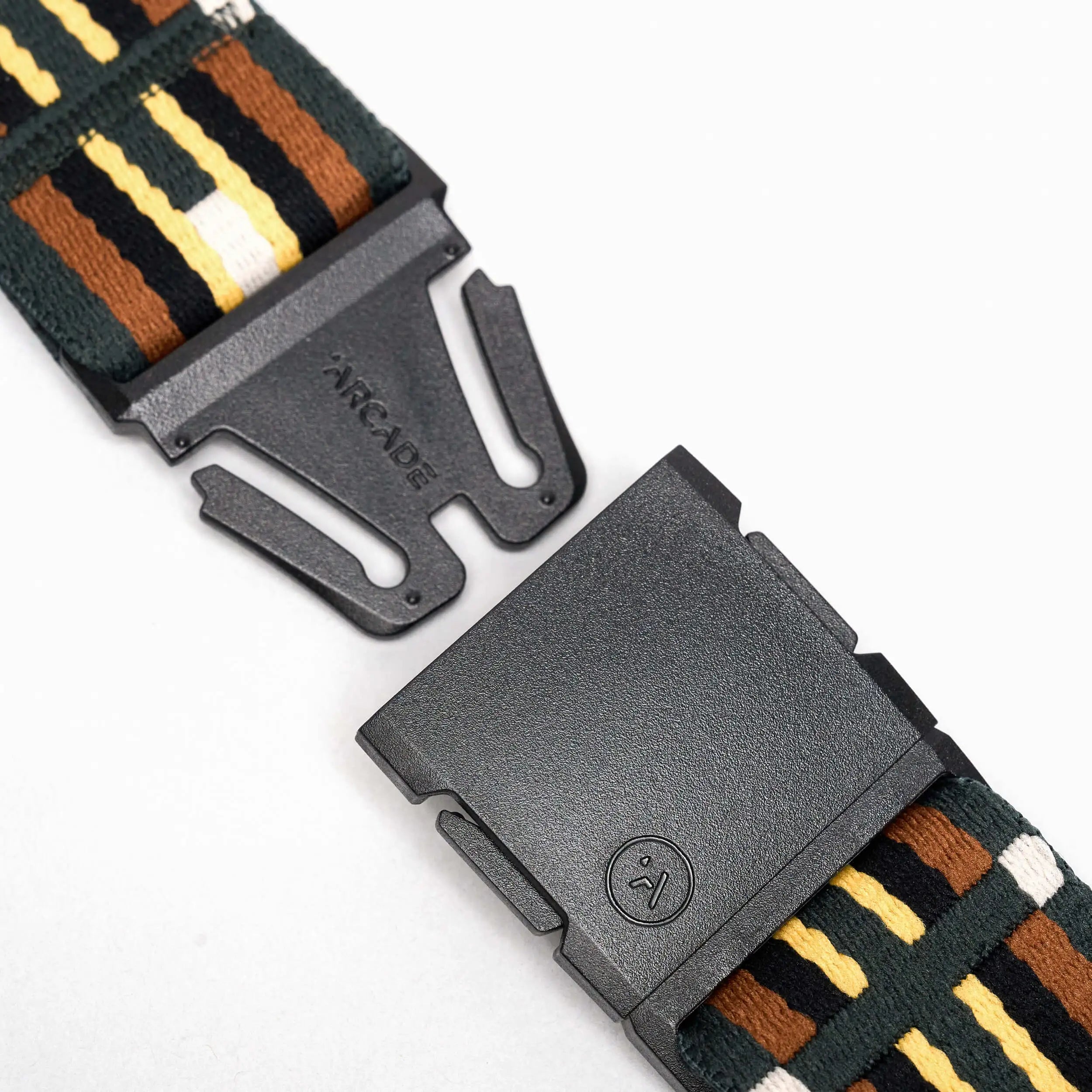 Close-up of a black plastic buckle on a Vernan Kee by Arcade Belts strap with green, yellow, white, and brown stripes. The partially unclasped buckle features the word ARCADE.