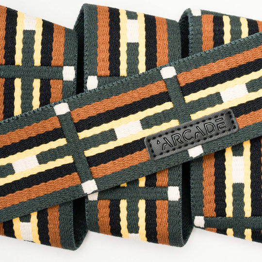 A close-up of the Vernan Kee Elastic Stretch Belt by Arcade Belts, with brown, black, yellow, and white geometric stripes, a stitched black ARCADE label, and flexible stretch webbing.