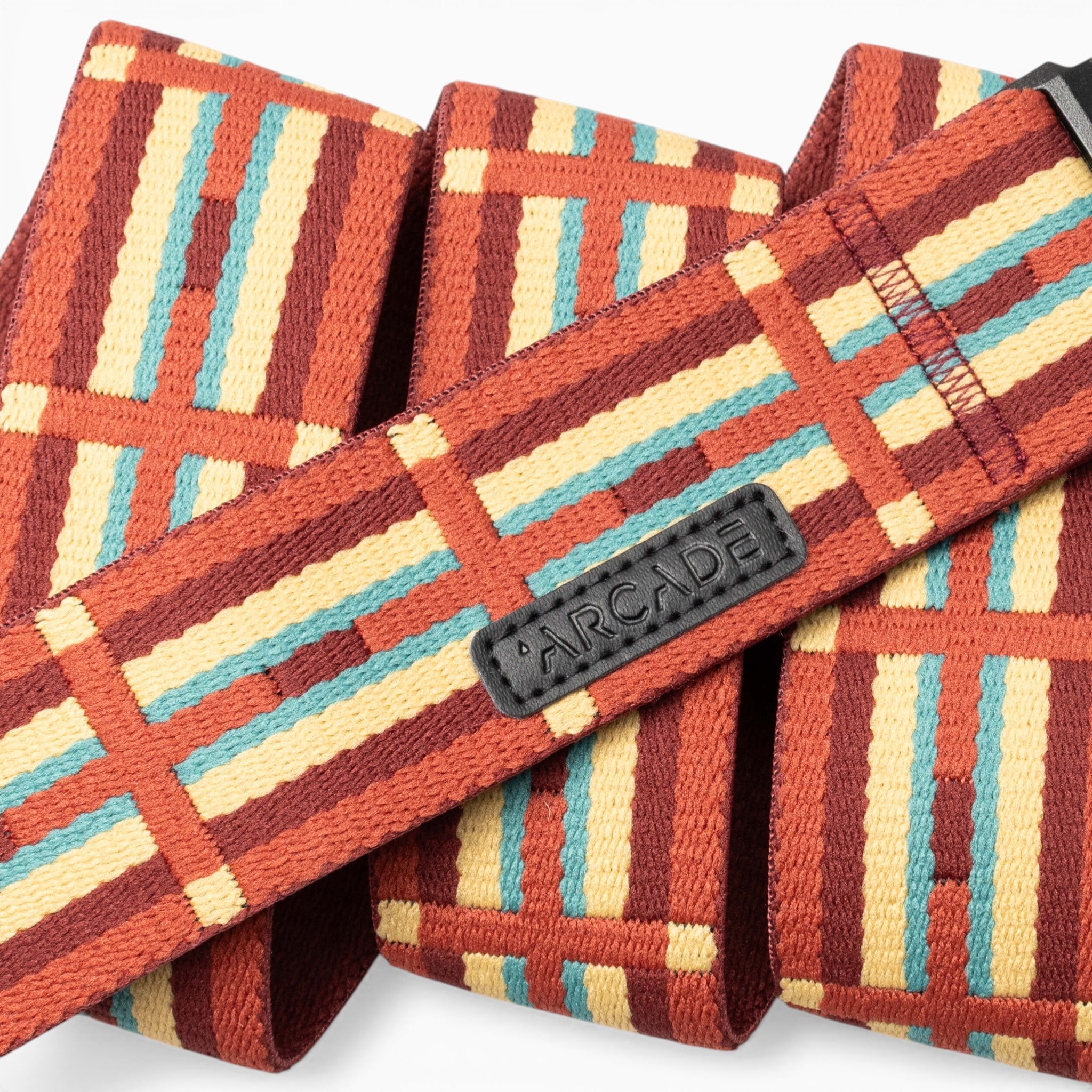 A close-up of the Vernan Kee belt by Arcade Belts showcases geometric shapes inspired by Navajo rug patterns in red, yellow, turquoise, and brown. The black Arcade label is stitched onto the belt, highlighting Vernan Kee’s artistic influence.
