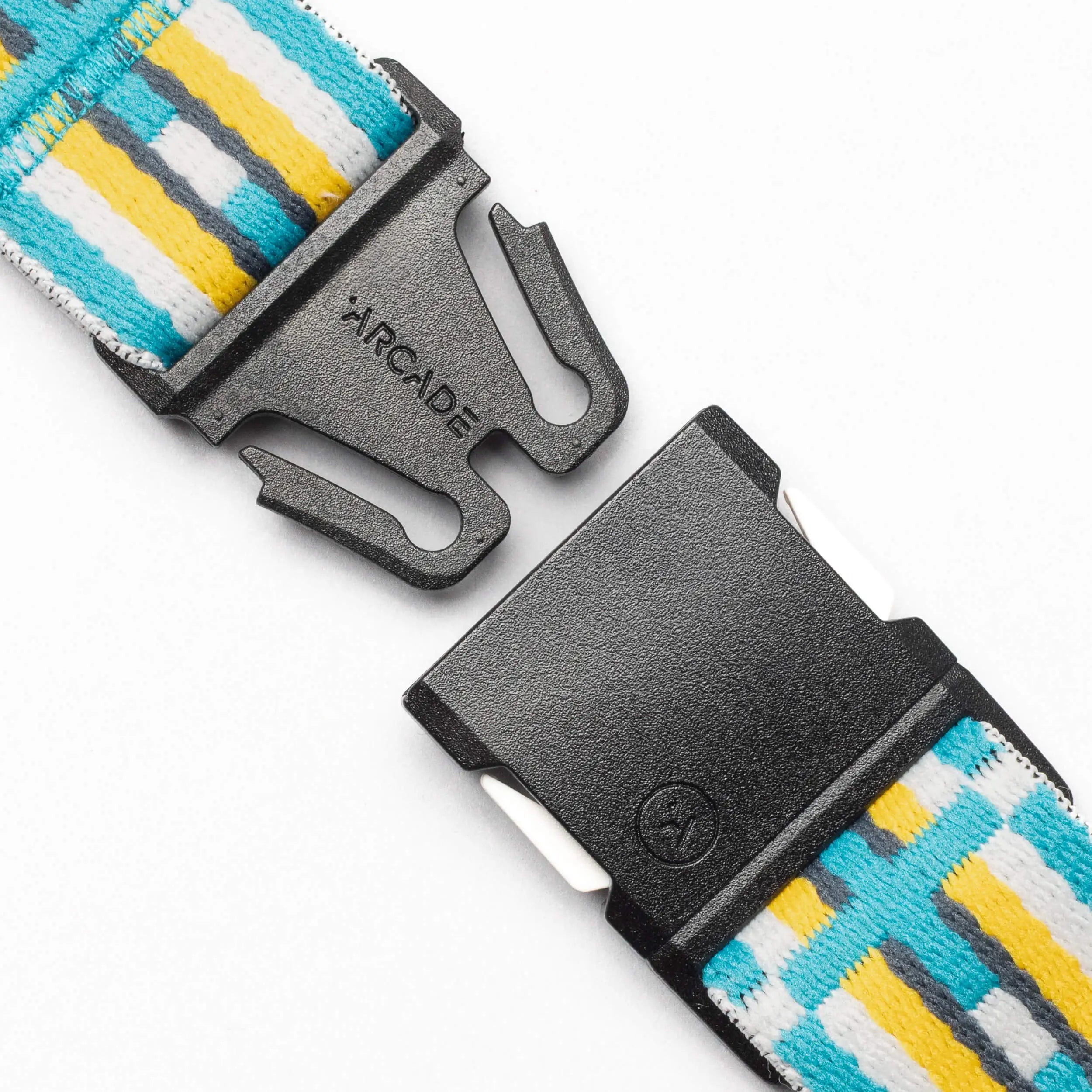 Close-up of a black plastic buckle on the Arcade Belts Vernan Kee strap, showcasing colorful geometric patterns in yellow, blue, and white stripes. The brand name Arcade is visible on one side of the buckle.