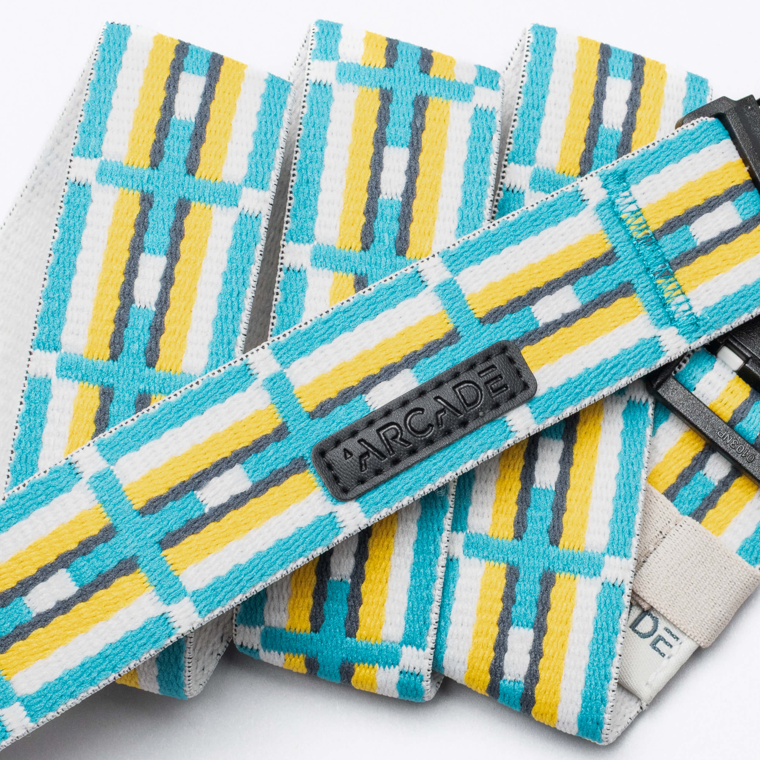 A close-up of the Vernan Kee belt by Arcade Belts, featuring yellow, white, turquoise, and gray geometric patterns inspired by Navajo rugs. A black patch displays the Arcade Belts logo in raised letters.